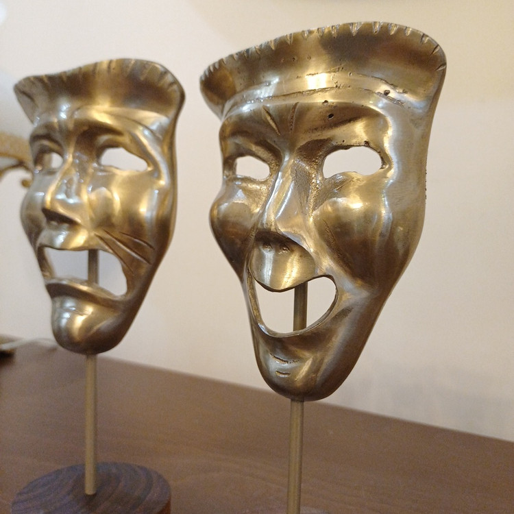 Close-up of the laugh and cry comedy-tragedy mask design on aluminum sculpture with wooden base