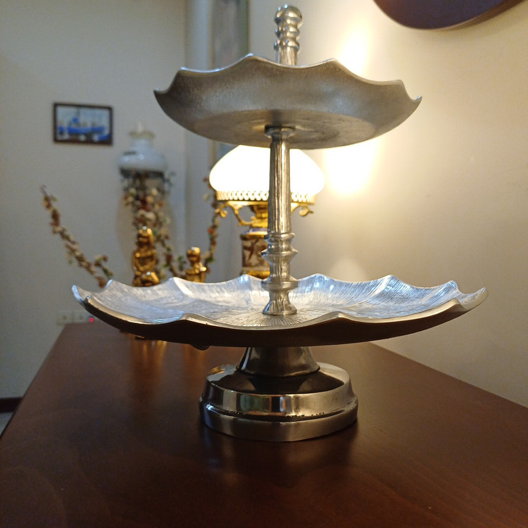 Decorative two-tier pedestal serving stand made of aluminum with sleek linear detailing and metallic finish.