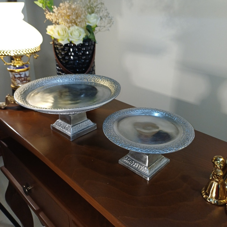 “Pair of hammered aluminum pedestal bowls. Rustic yet elegant design, perfect for adding texture and shine to any table setting.”