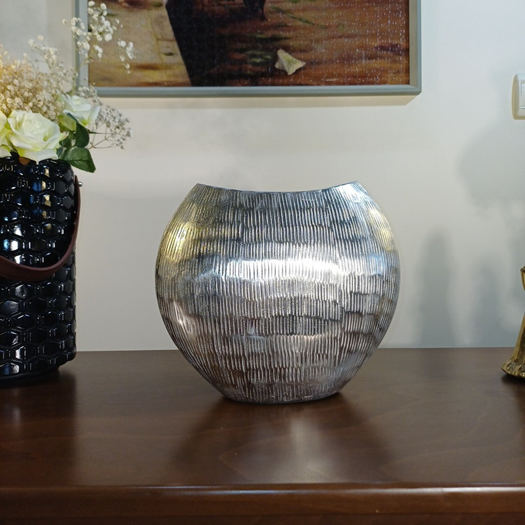 “The ‘Mahtab’ vase: an abstract aluminum decorative piece. Features a smooth, metallic finish with subtle vertical texturing and a sculptural handle.”