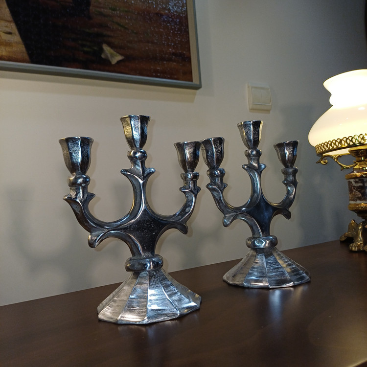 Three-arm aluminum candlestick holder with burning taper candles, creating a warm ambiance in a luxury home interior.